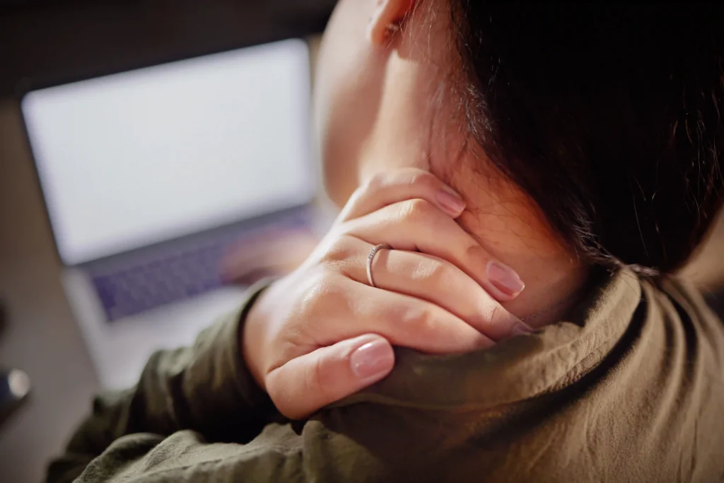 Woman experiencing a stiff neck while sitting at a desk